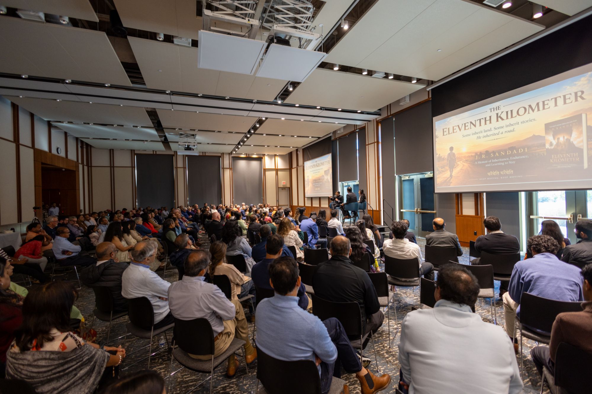 A full room in Carmel, Indiana, listening to J. R. Sandadi in conversation on stage, with The Eleventh Kilometer on the screens